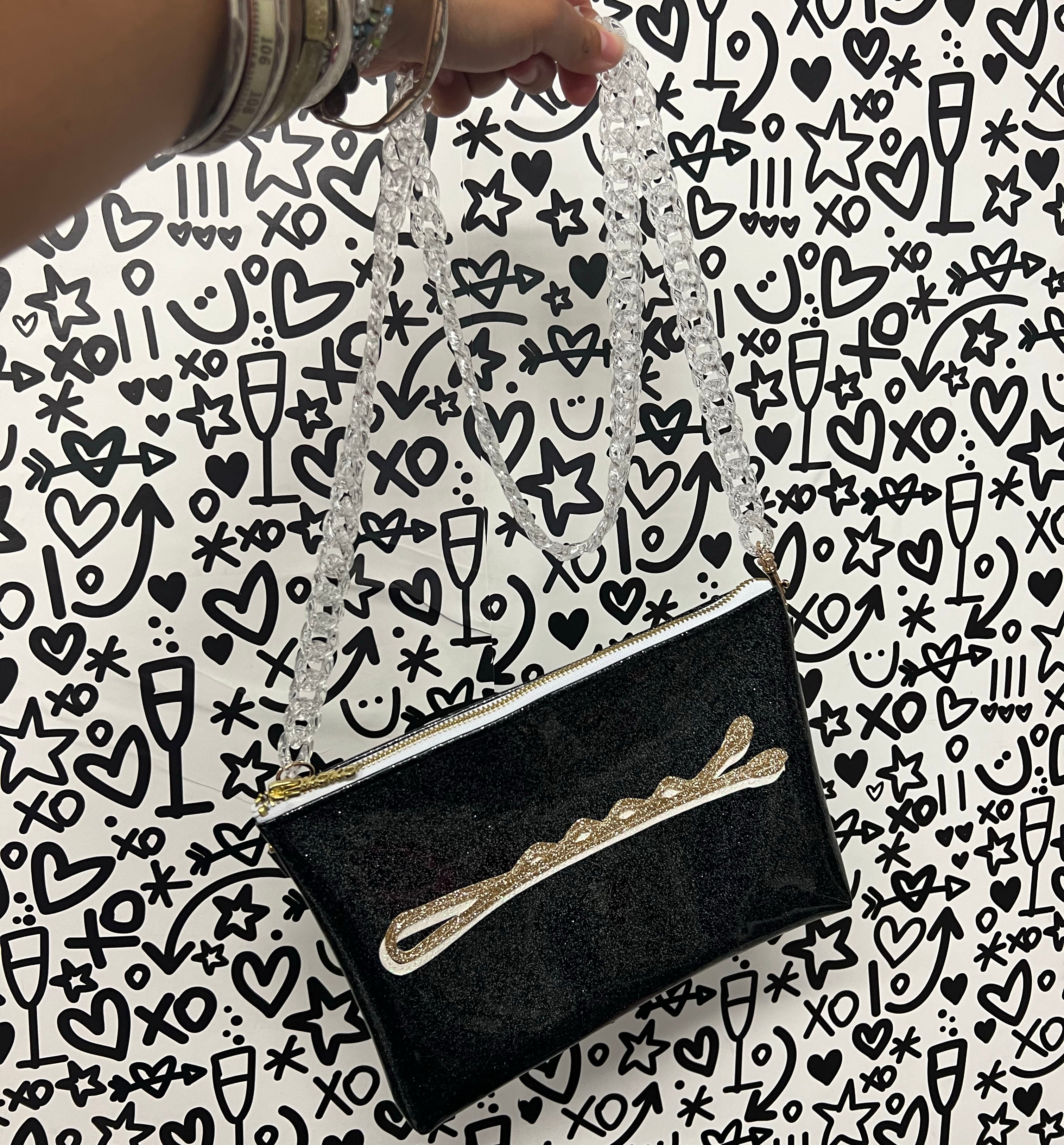 Customizable crossbody bag that features a bobby pin applique in gold and white sparkly canvas on a black glitter infused vinyl. Crossbody strap is a clear acrylic chain. 