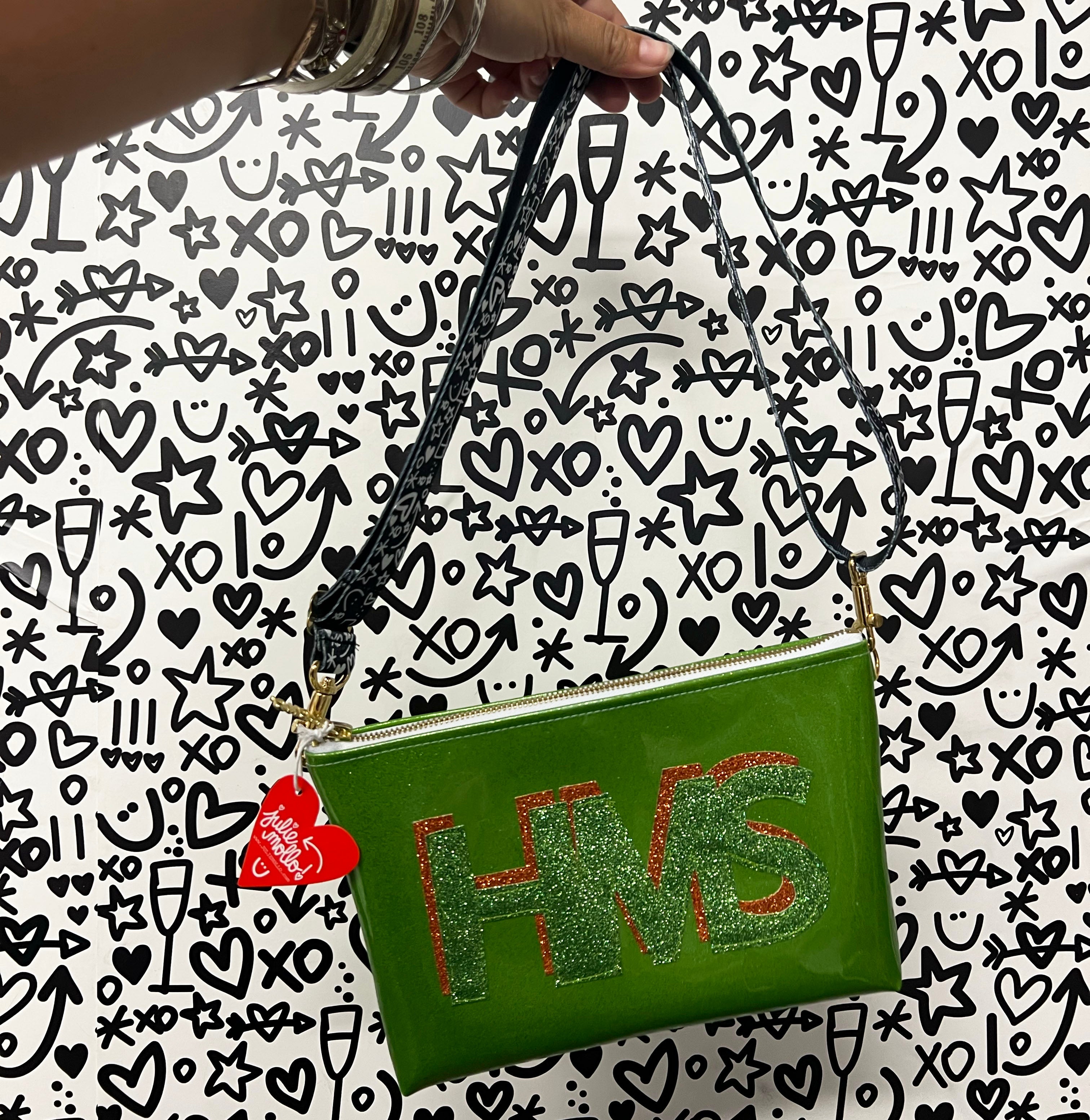 Customizable crossbody bag that features "HMS" initial applique in red and green sparkly canvas on a green glitter infused vinyl. Crossbody strap is black nylon with white Julie Mollo doodles. 