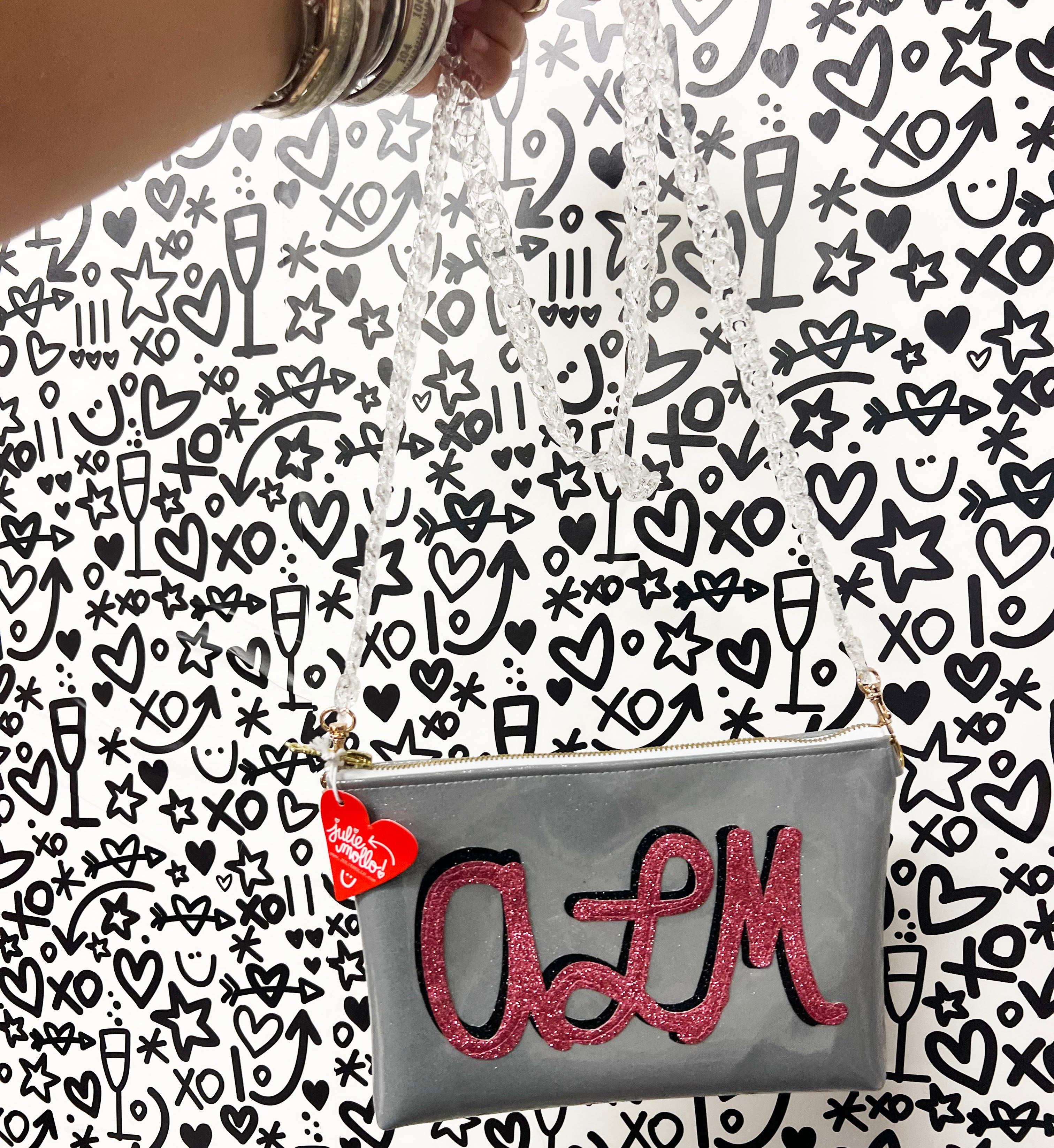 Customizable crossbody bag that features "ALM" initial applique in pink and black sparkly canvas on a silver glitter infused vinyl. Crossbody strap is a clear acrylic chain. 