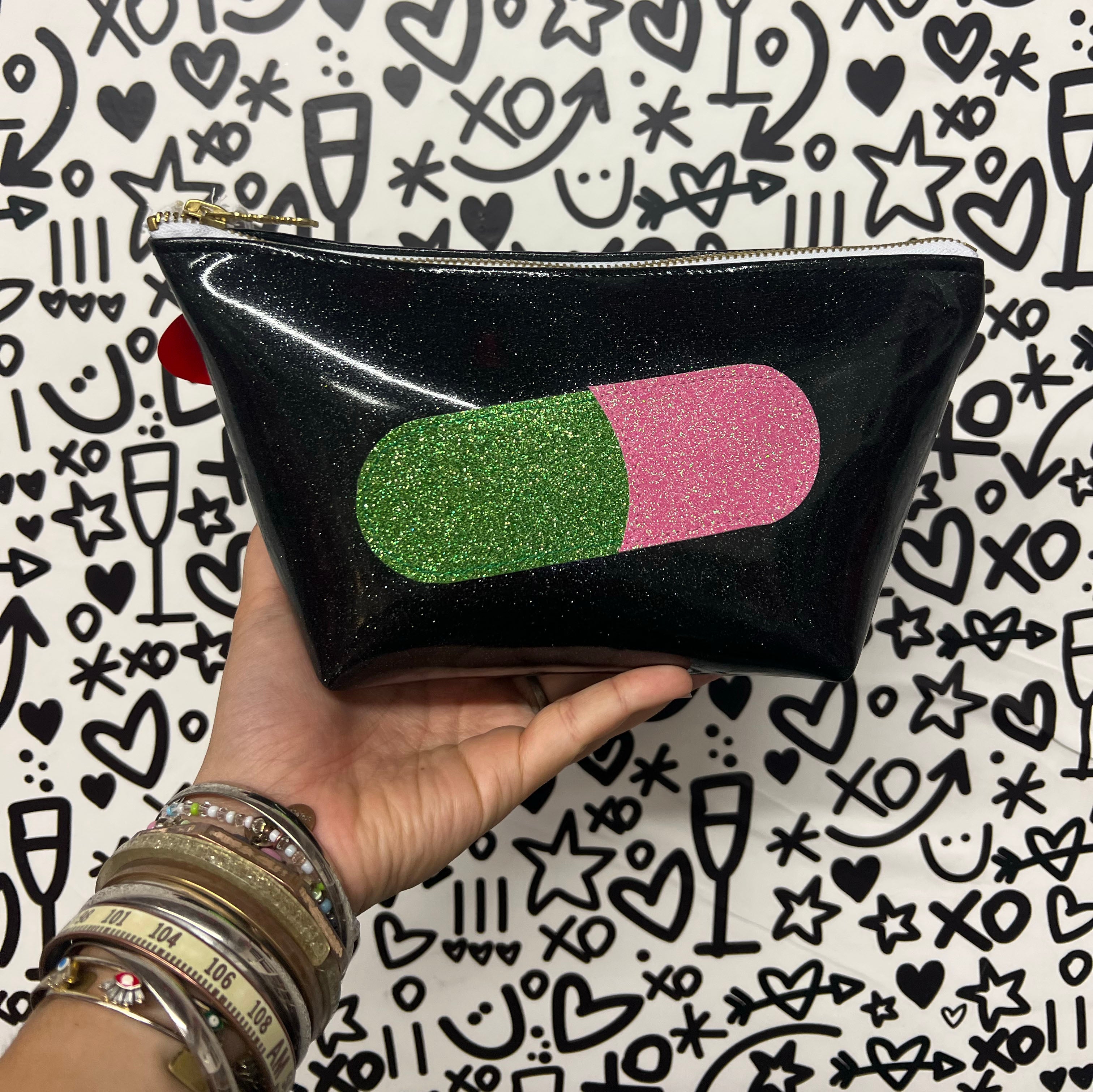 Black glitter infused pouch with a green and pink glittery pill applique on the front. 