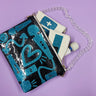 Shoulder bag with blue Magic Wand doodle appliqués from Julie's custom MW doodle print sewn onto black sparkle glitter vinyl and coated with a clear vinyl. Shoulder strap is a clear acrylic chain. Coming out of bag are smaller clutches and a Magic Wand vibrator. 