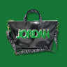 black glittery vinyl tote bag with the name "Jordan" in bold green and white letters on the front. The bag features a removable shoulder strap with a fun, doodle-inspired pattern of stars, hearts, and shapes.