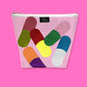 Cute clear vinyl travel bag with sparkly and colorful pills scattered about the bag. On top of the bag is a zipper with a Julie Mollo custom XOXO zipper pull. Bag is pictured on  a pink background. 