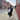 Julie Mollo standing on a NYC sidewalk wearing a black winter puffer jacket while holding a red glittery vinyl clutch that features fun NYC icons like pepperoni, a yellow cab, a golden street pretzel, and a lime green Statue of Liberty. 