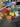 Hand holding a Cute clear vinyl travel bag with sparkly and colorful pills scattered about the bag. On top of the bag is a zipper with a Julie Mollo custom XOXO zipper pull in front of a busy and fun studio background. 